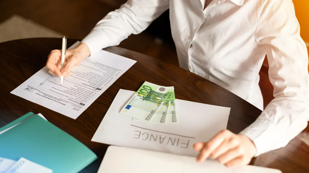 Person gennemgår budgetpapirer med eurokontanter på bordet